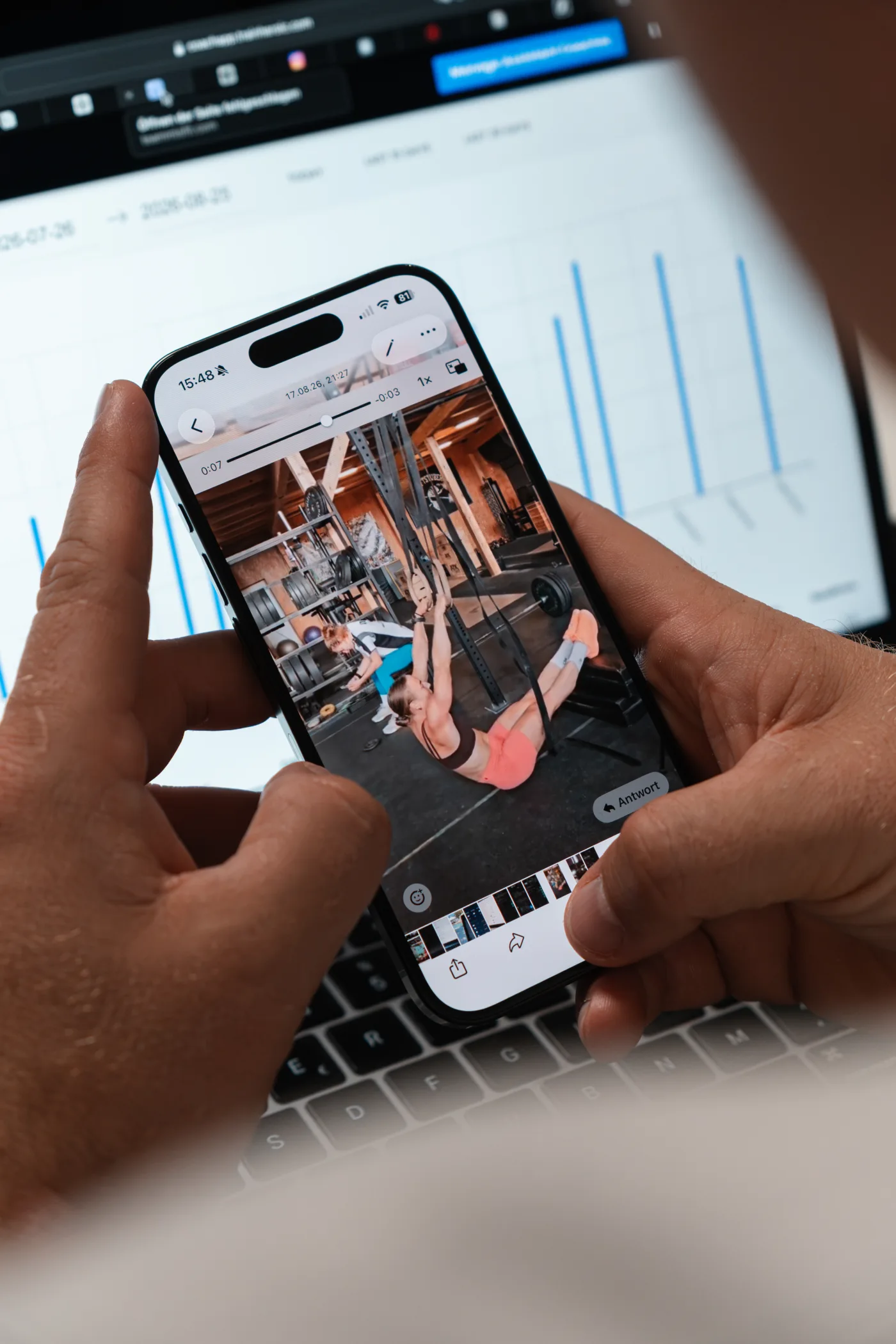 Alexander Panskus prüft ein Trainingsvideo am Smartphone vor einem geöffneten Laptop